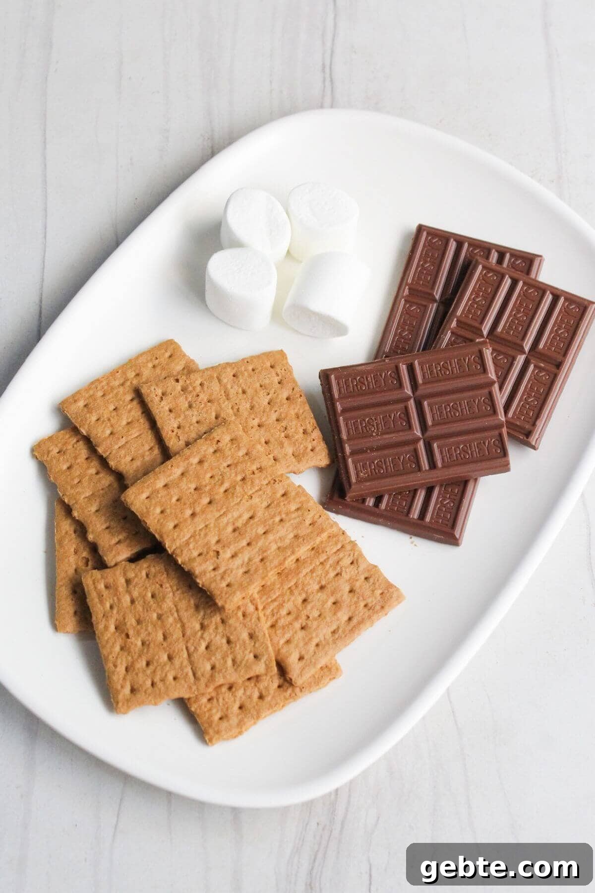 Crispy Air Fryer S'mores Recipe: Gooey Campfire Treats Fast 3 Graham crackers, marshmallows and chocolate bars on a white plate.