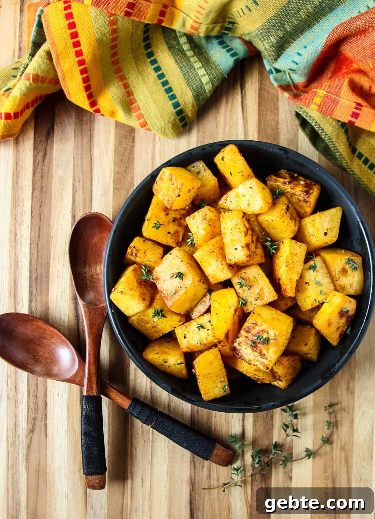 Roasted rutabaga cubes in a black bowl  and two wooden spoons on a wooden board.