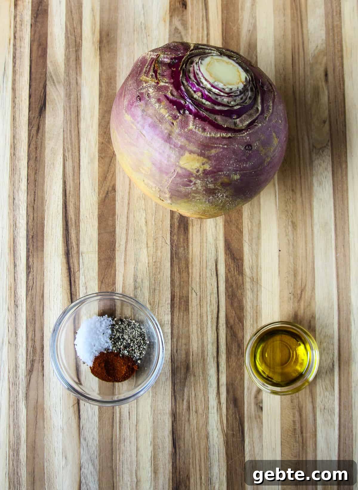 A whole raw rutabaga on a cutting board with a small bowl of seasonings and a small dish of oil. 