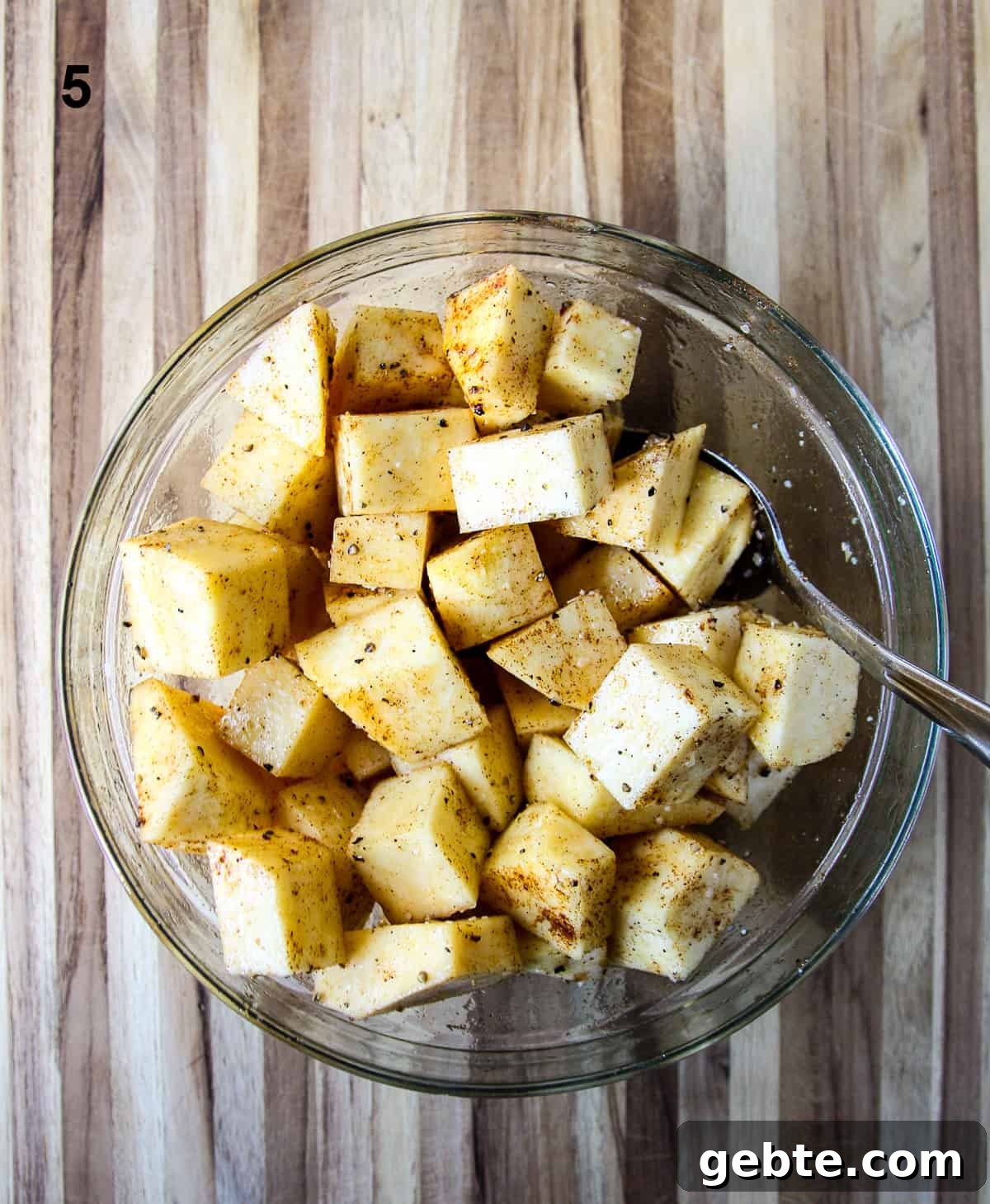 The cut  cubes being tossed with seasoning and oil in a glass bowl.