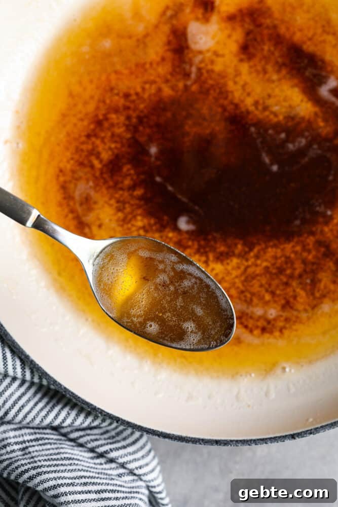 Spoon lifting browned butter from a skillet. Close up view of a spoon lifting up brown butter out of a white skillet. A blue and white striped towel is next to the skillet.