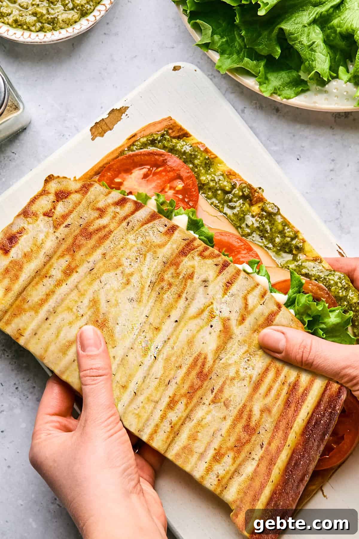 Protein-Packed Cottage Cheese Flatbread (Gluten-Free, Flourless) 2 cottage cheese flatbread with turkey, tomato, lettuce and pesto with 2 hands holding it on a cutting board