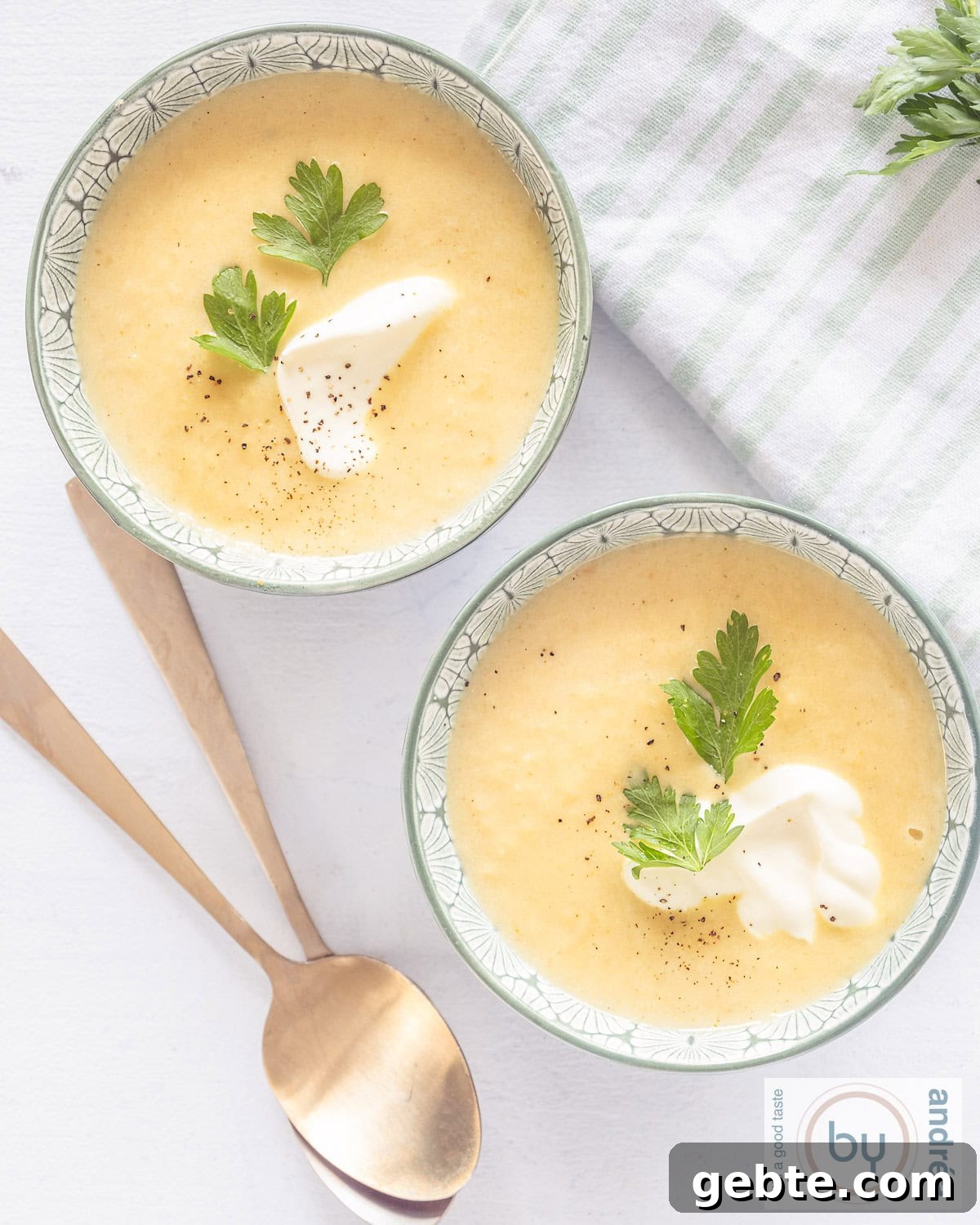A top-down photo of two bowls filled with parsnip soup with yogurt and cilantro. Two golden spoons lie beneath them.