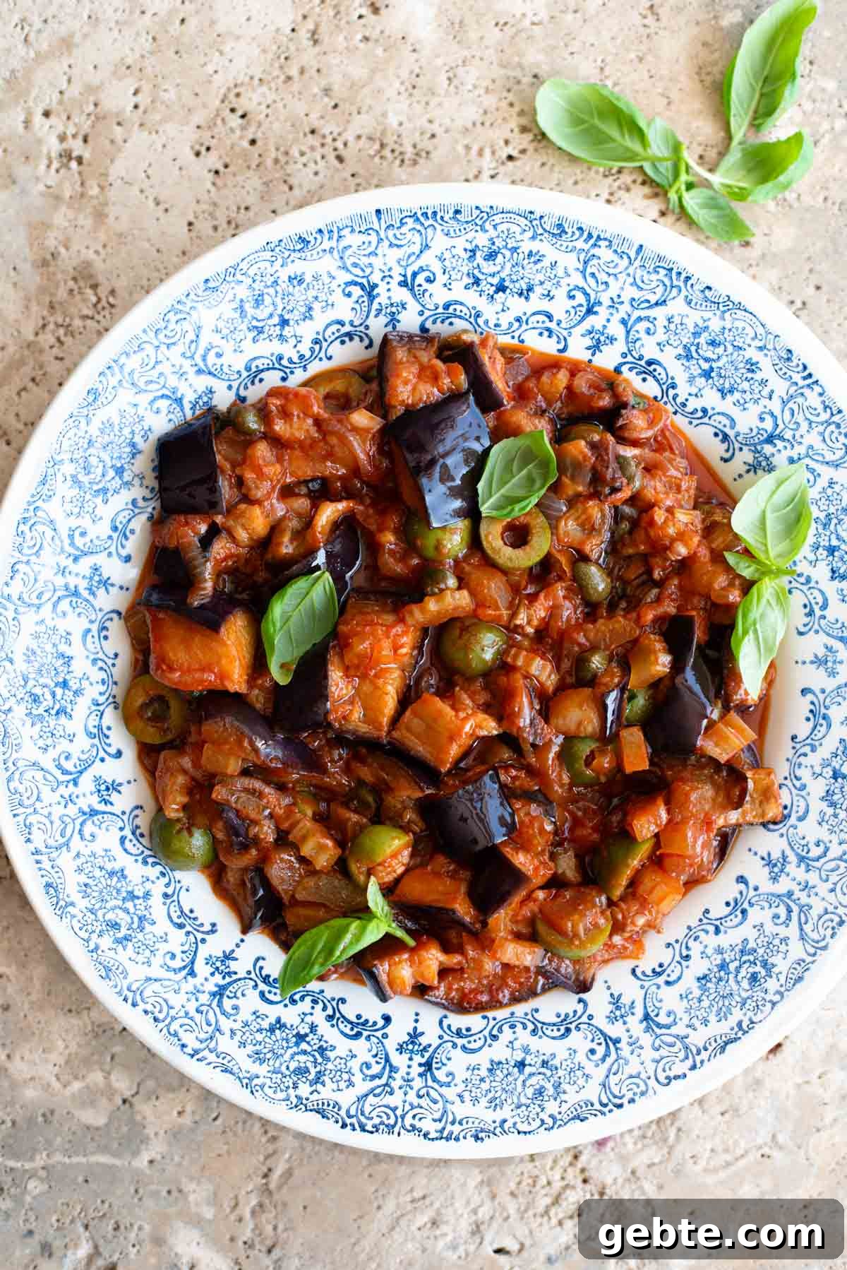 Sicilian Eggplant Caponata Recipe: Authentic Sweet-Sour Relish 2 Sicilian caponata in a blue patterned bowl sitting on a travertine surface.