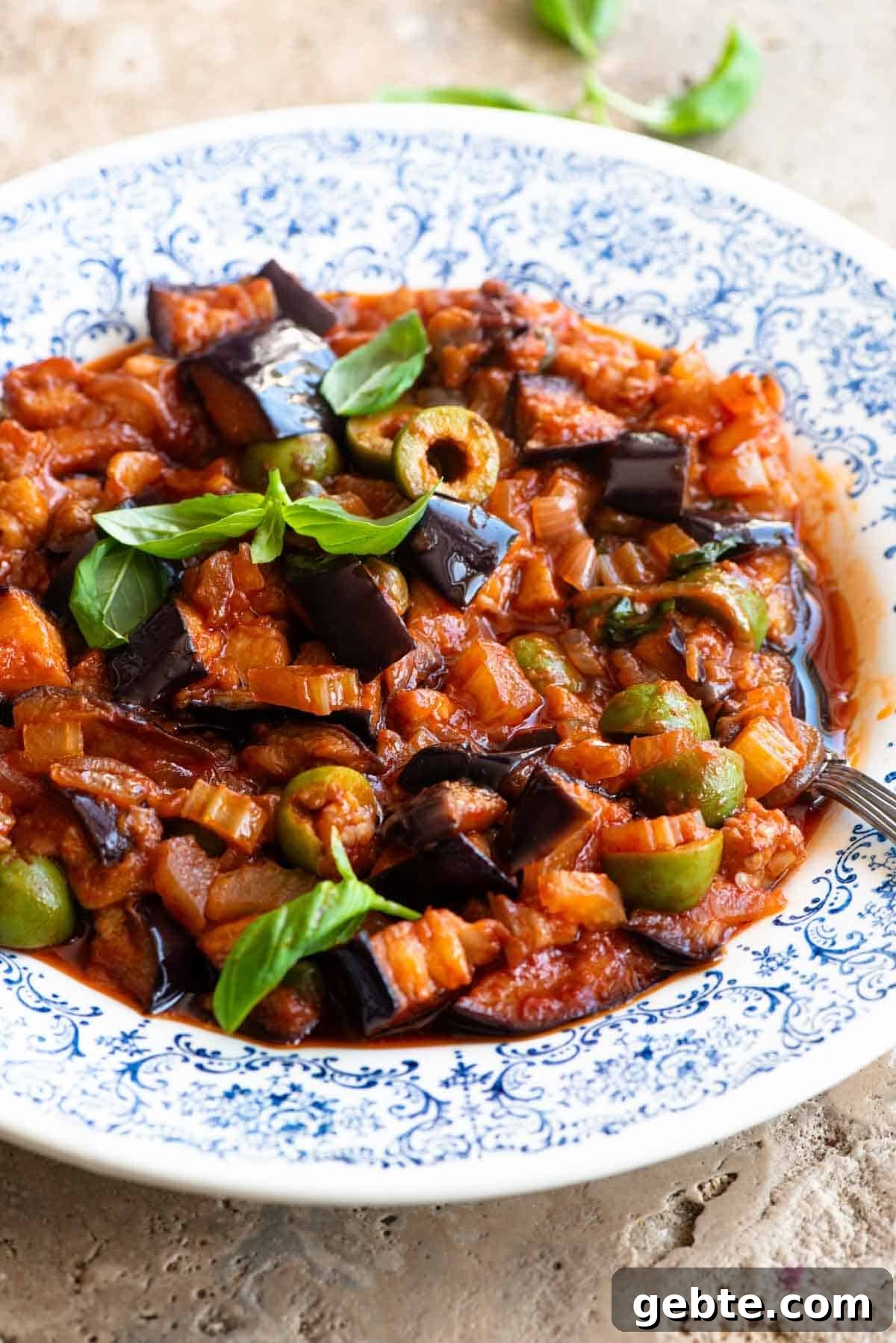 Sicilian Eggplant Caponata Recipe: Authentic Sweet-Sour Relish 7 A side shot of caponata in a blue and white bowl topped with fresh basil leaves.