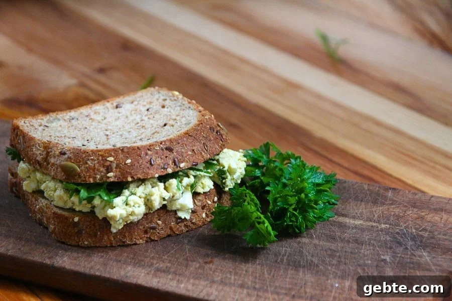 an egg salad sandwich sitting on a wooden cutting board with green parsley on the side