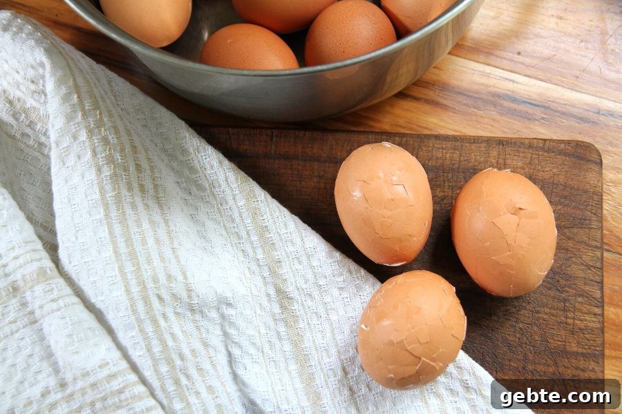 The boiled eggs with mashed shells sitting on a cutting board next to a stainless steel pot of eggs