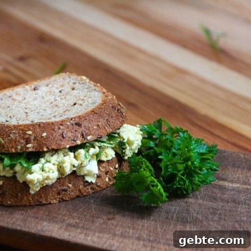 an egg salad sandwich sitting on a wooden cutting board with green parsley on the side