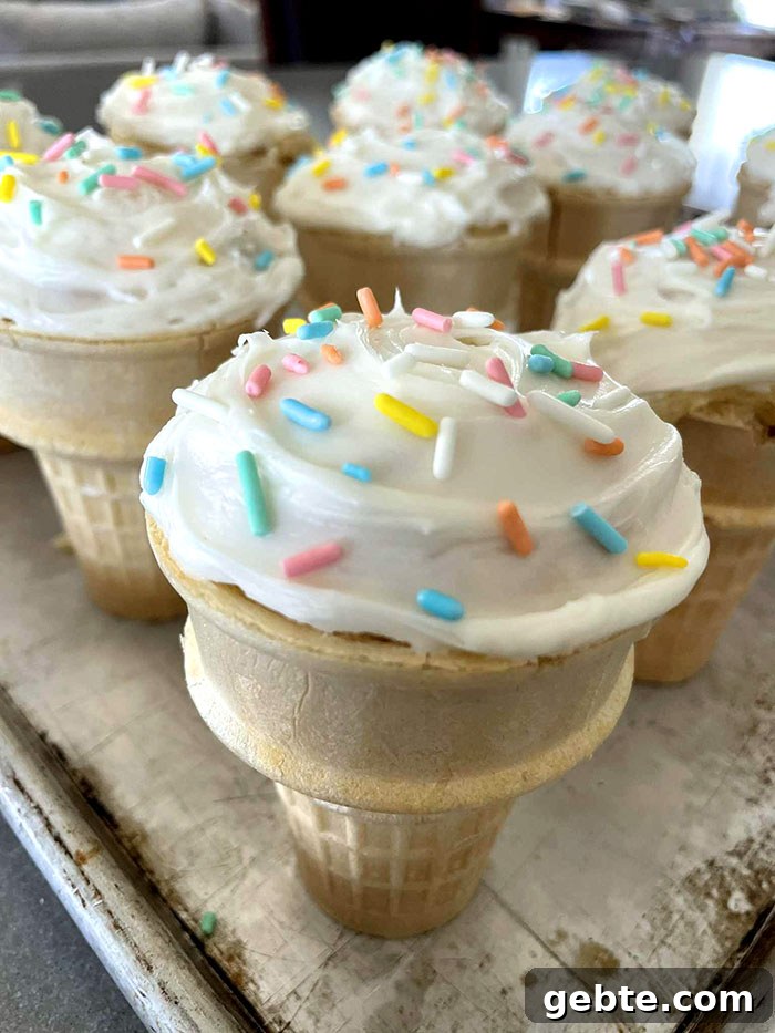 A baking sheet filled with ice cream cone cupcakes with vanilla frosting and sprinkles.