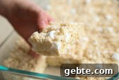 A glass 9x13 dish of cut Rice Krispie Treats with one piece held above by a hand.