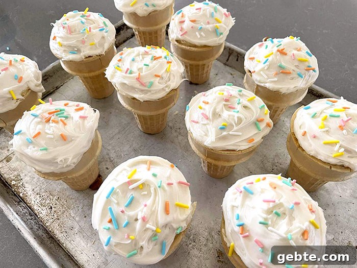 A large baking sheet with cupcake cones frosted with vanilla frosting and topped with multicolored sprinkles.