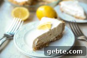 Two small white plates stacked on each other with a slice of three ingredient lemonade ice cream pie with a lemon wedge on top.