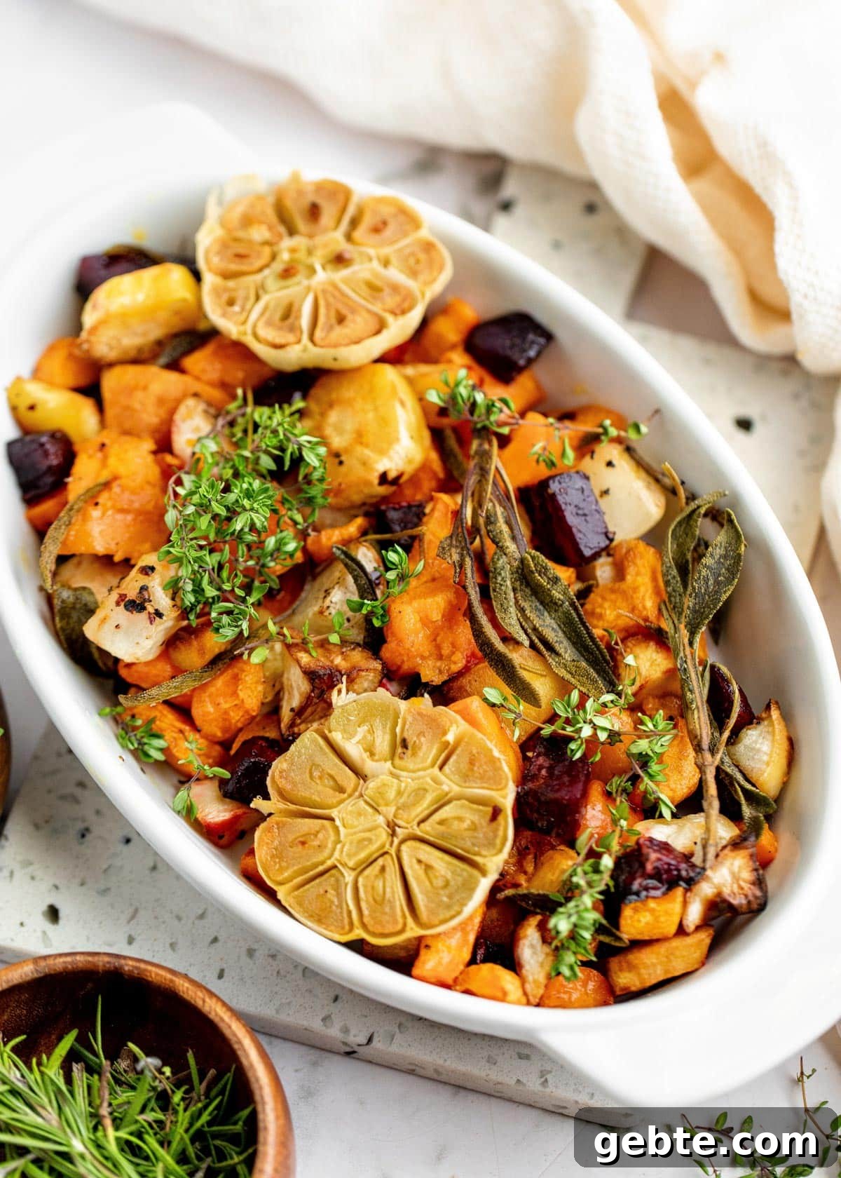 roasted assorted root vegetables in a white gratin dish garnished with fresh herbs