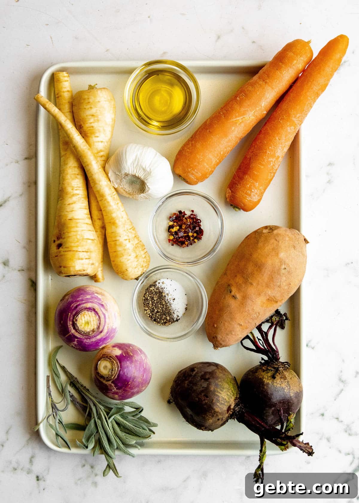 overhead photo of raw root vegetables on a baking sheet, with bowls of olive oil and seasonings