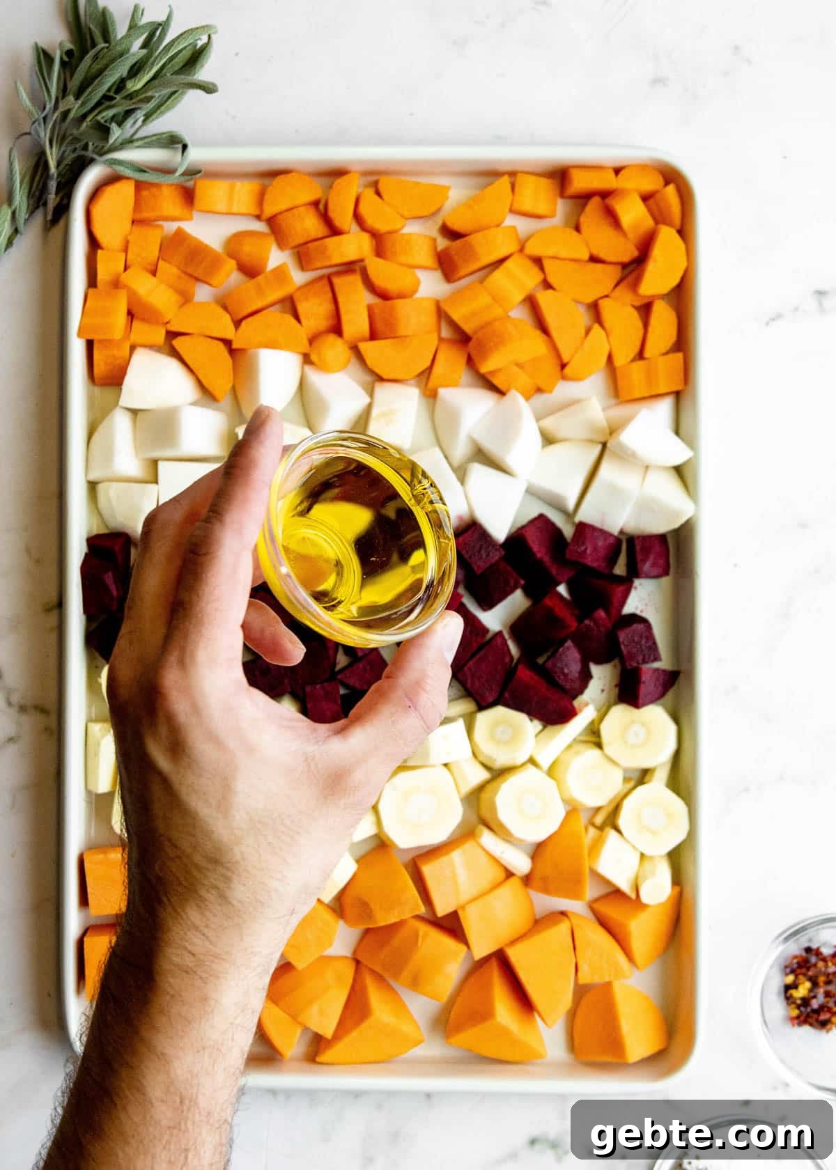 overhead photo of olive oil being drizzled over cubed root vegetables on a baking sheet