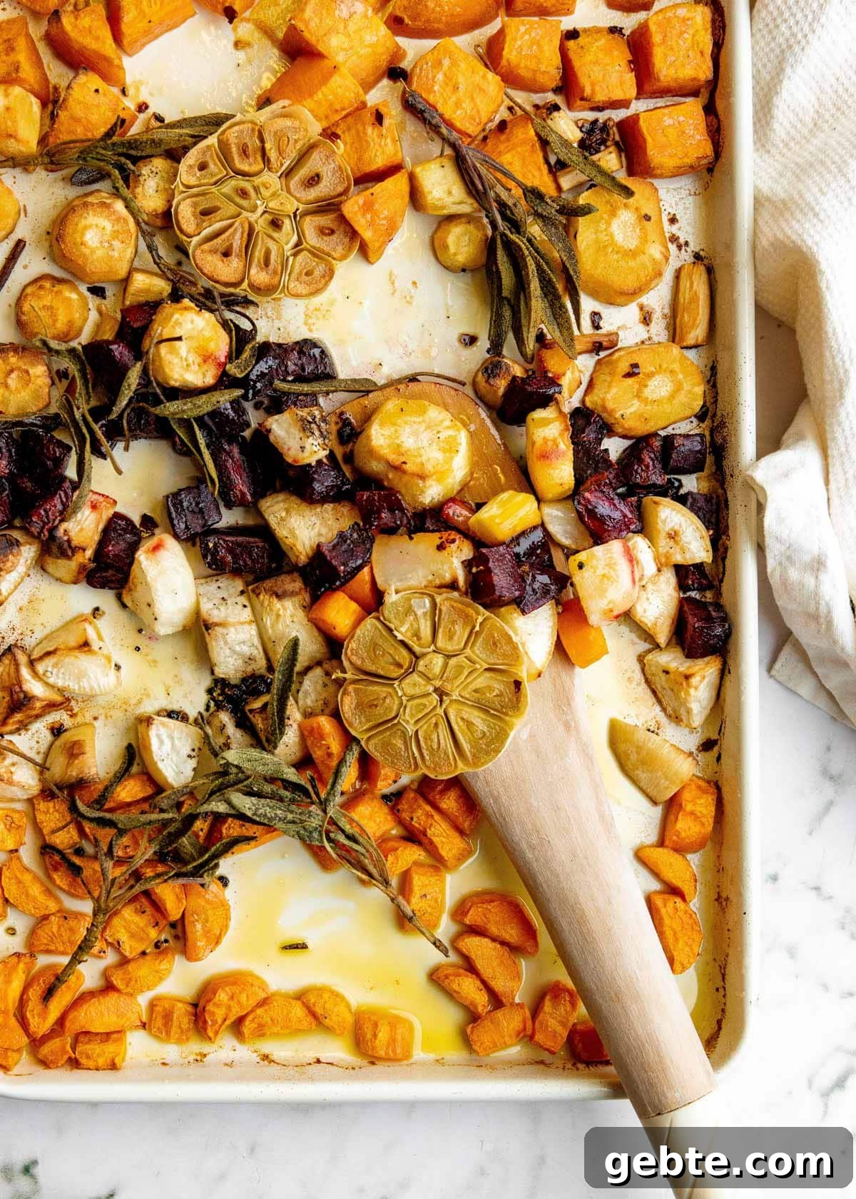 cooked roasted root vegetables on a baking sheet with a wooden spoon