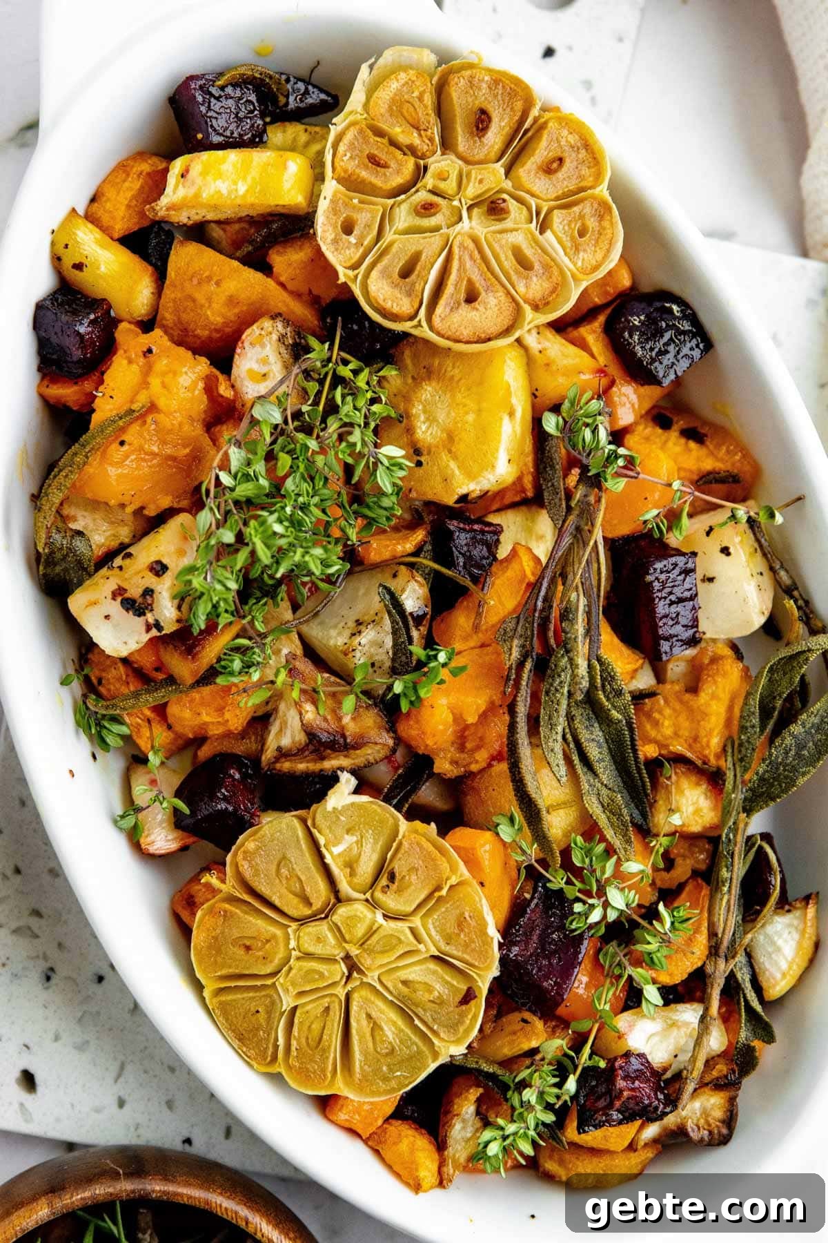 overhead photo of roasted root vegetables in a white gratin dish, garnished with fresh herbs