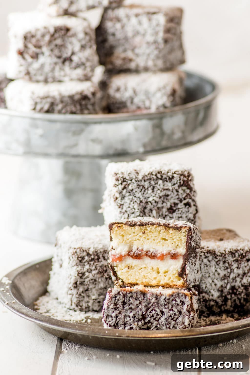 Lamingtons stacked on a rustic pin tin on a white rustic wooden board.