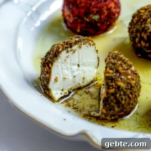 A close-up shot of a labneh ball coated in za'atar sliced in half to show the stark white, dense, and creamy yogurt cheese interior on a white plate with olive oil.
