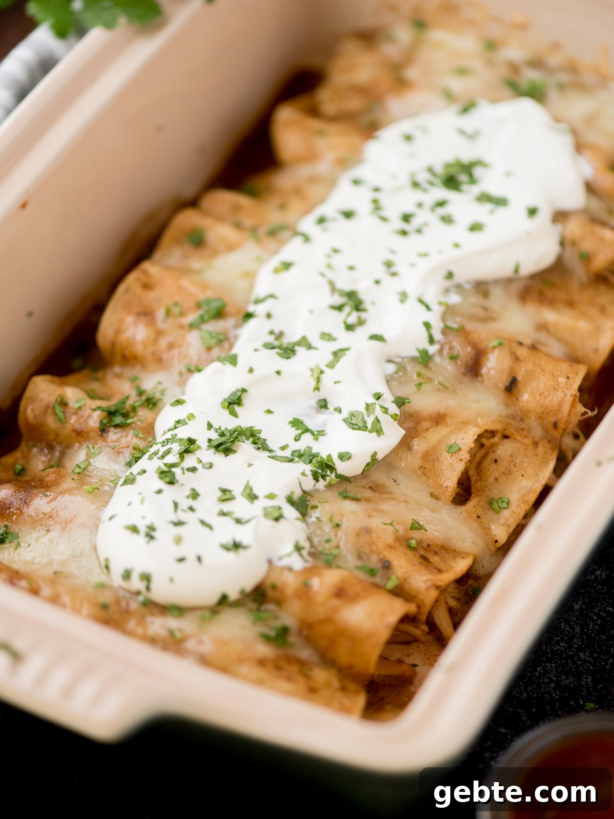Authentic Red Chicken Enchiladas Recipe with Homemade Sauce 2 chicken enchiladas in a baking dish topped with sour cream and fresh cilantro