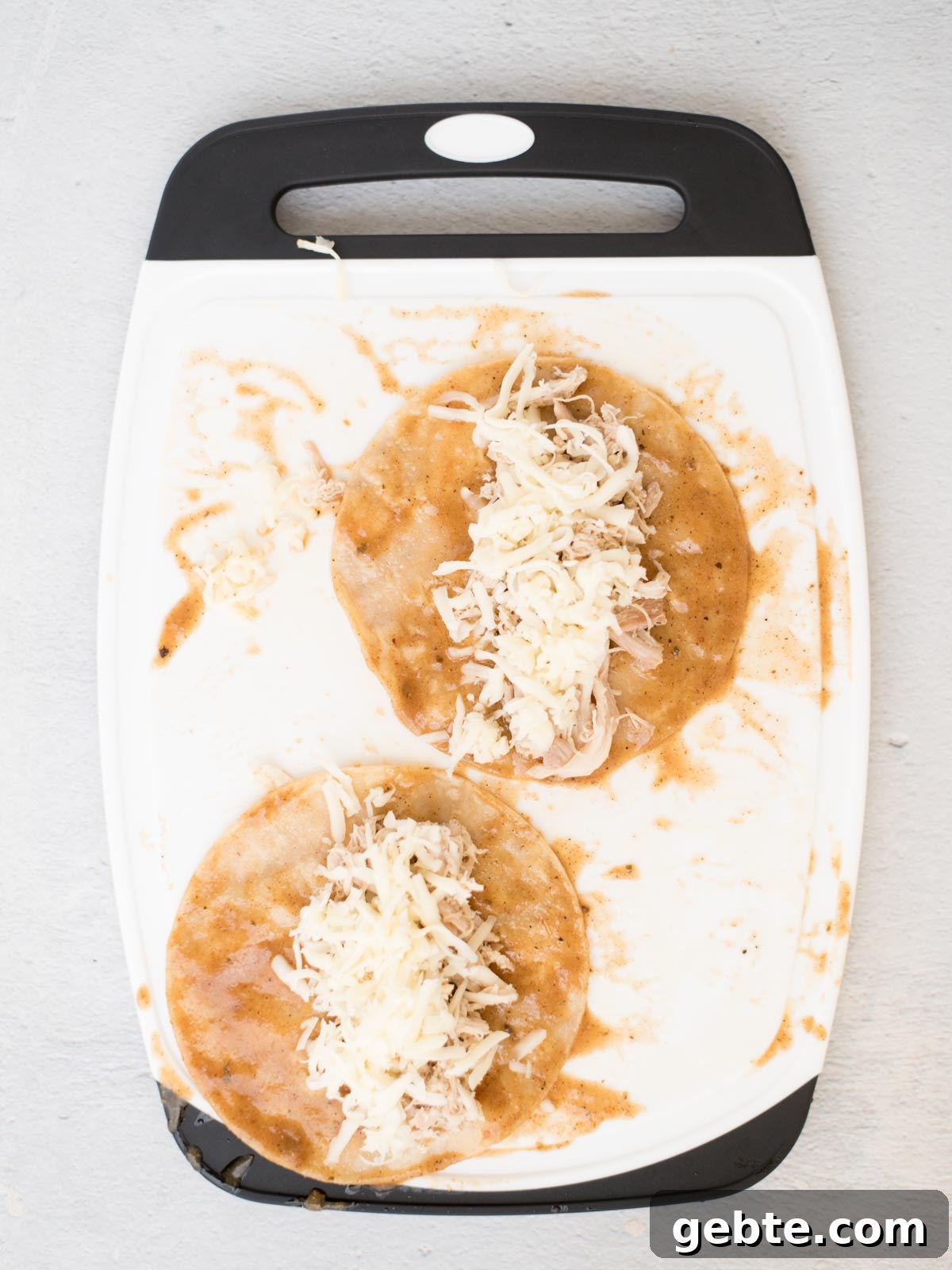 Authentic Red Chicken Enchiladas Recipe with Homemade Sauce 12 cheese and chicken on top of sauced tortillas on a cutting board