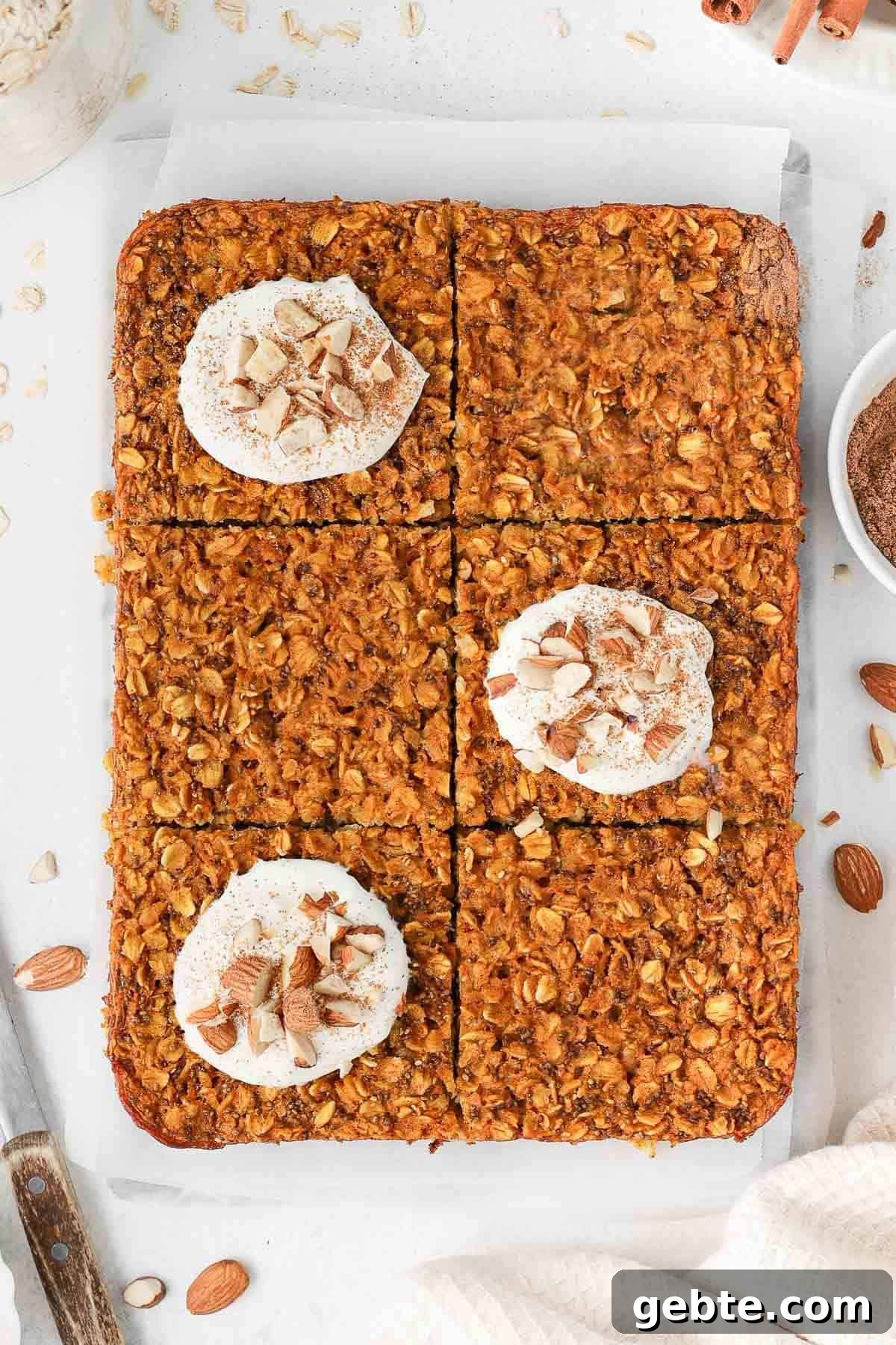 Baked oats cut into six pieces, three pieces topped with yoghurt and chopped nuts, sitting on some baking paper.