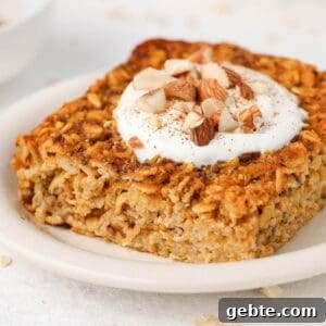 Slice of baked oats on a round white plate, topped with yoghurt and chopped almonds.