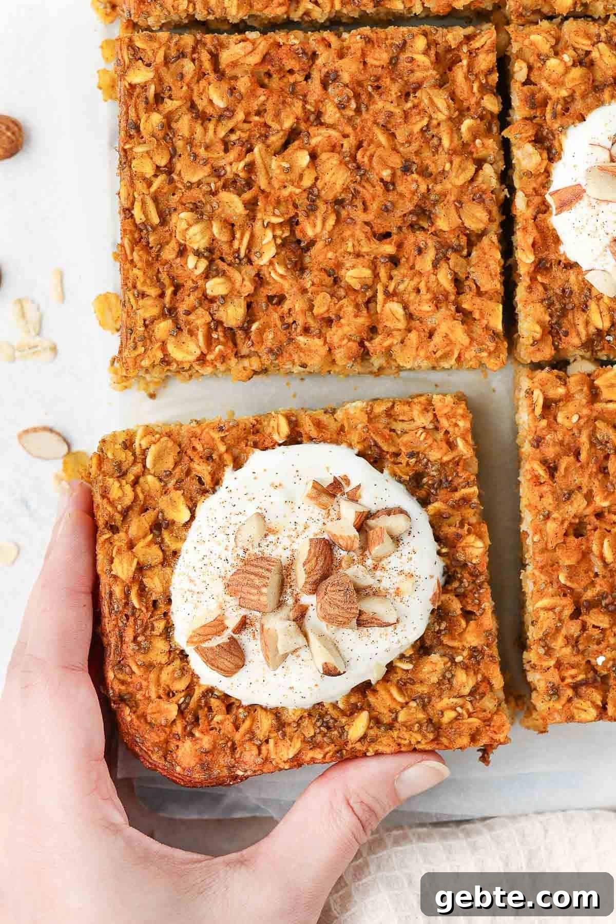 Hand reaching for a piece of baked oats which has been topped with yoghurt and nuts.