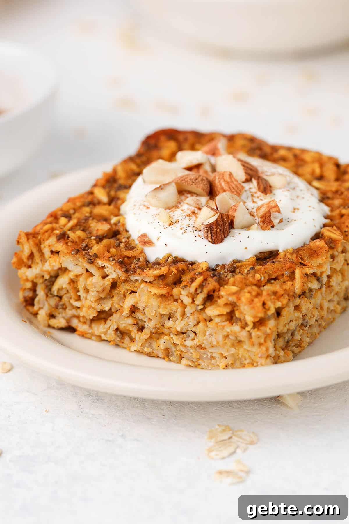 Slice of baked oats on a round white plate, topped with yoghurt and chopped almonds.