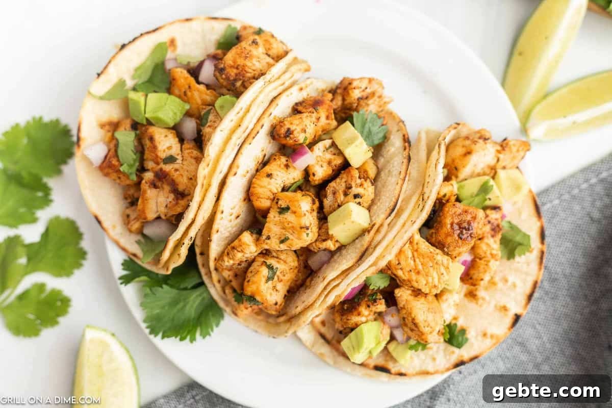 Crispy Blackstone Chicken Tacos with Charred Corn Salsa 2 Three Blackstone Chicken Tacos on corn tortillas, topped with diced avocado, red onion, and cilantro, served on a white plate with lime wedges and extra cilantro on the side.
