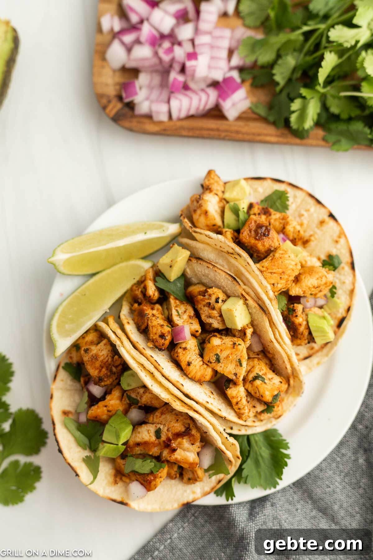 Crispy Blackstone Chicken Tacos with Charred Corn Salsa 6 3 chicken tacos on a plate topped with diced avocado and red onion with lime wedges on the side.