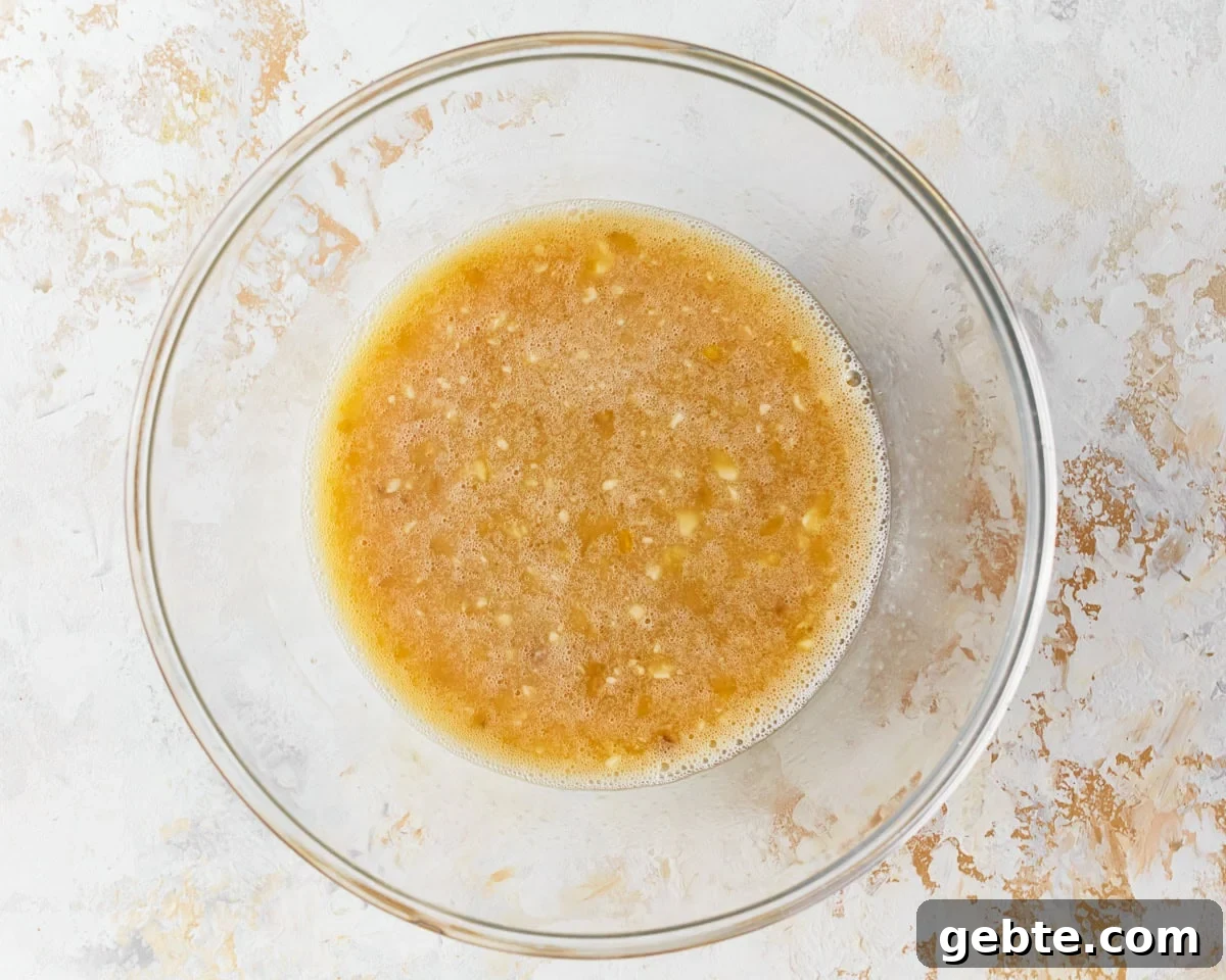 Mashed banana, coconut milk and oil, and honey added to a glass mixing bowl.