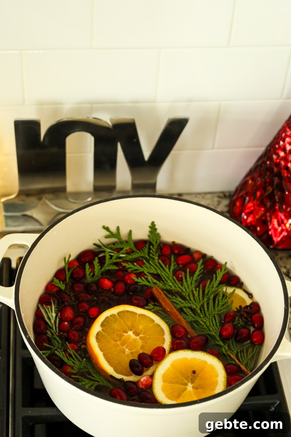 a cream colored pot of oranges, evergreen cutting, and cranberries on a stove top