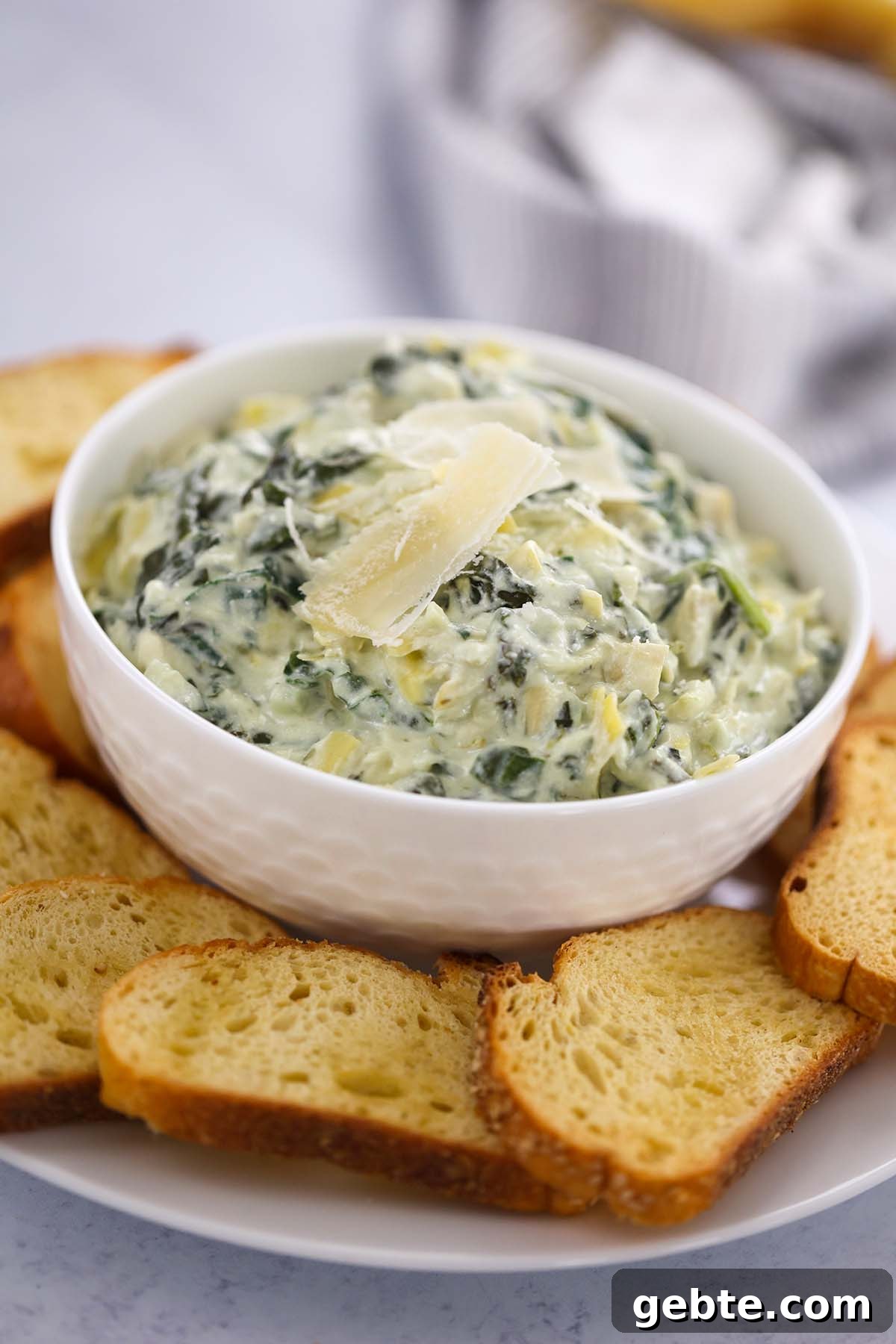 Slow Cooker Spinach and Artichoke Dip Recipe for Parties 2 Crockpot spinach artichoke dip in a white bowl with baguette slices.