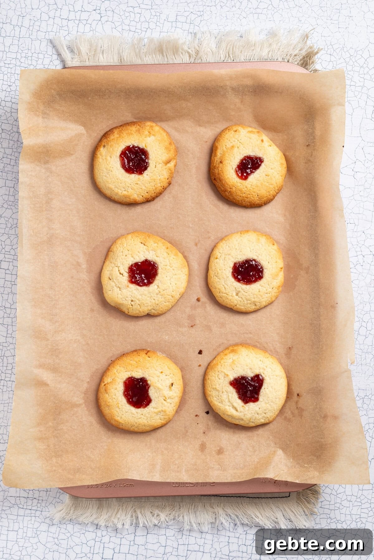 An overhead image of six baked cookies arranged side by side on a baking sheet with parchment paper.