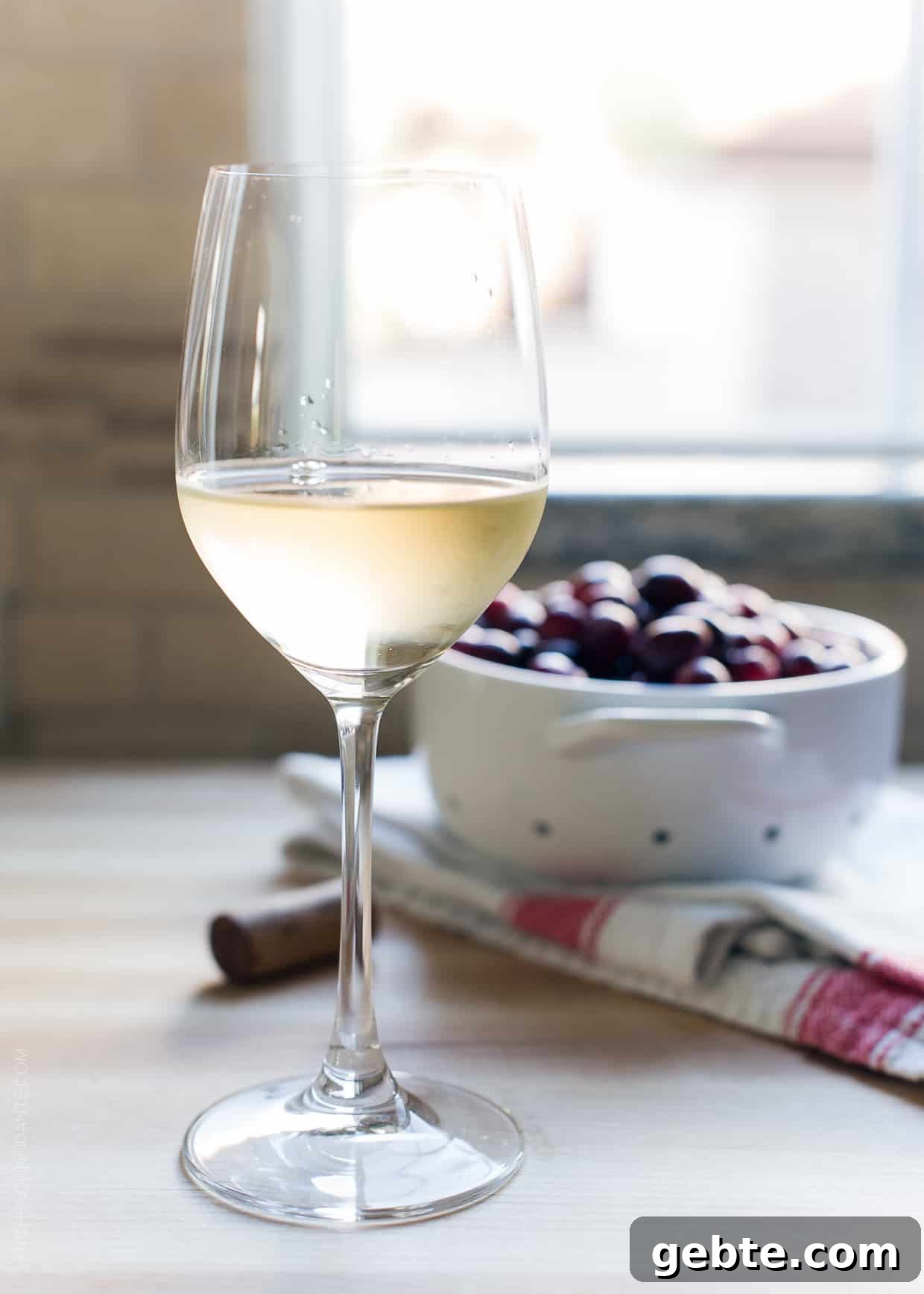 Cranberry Wine Sauce Recipe for Holiday Roasts and Sides 4 A glass of white wine with a bowl of cranberries in the background.