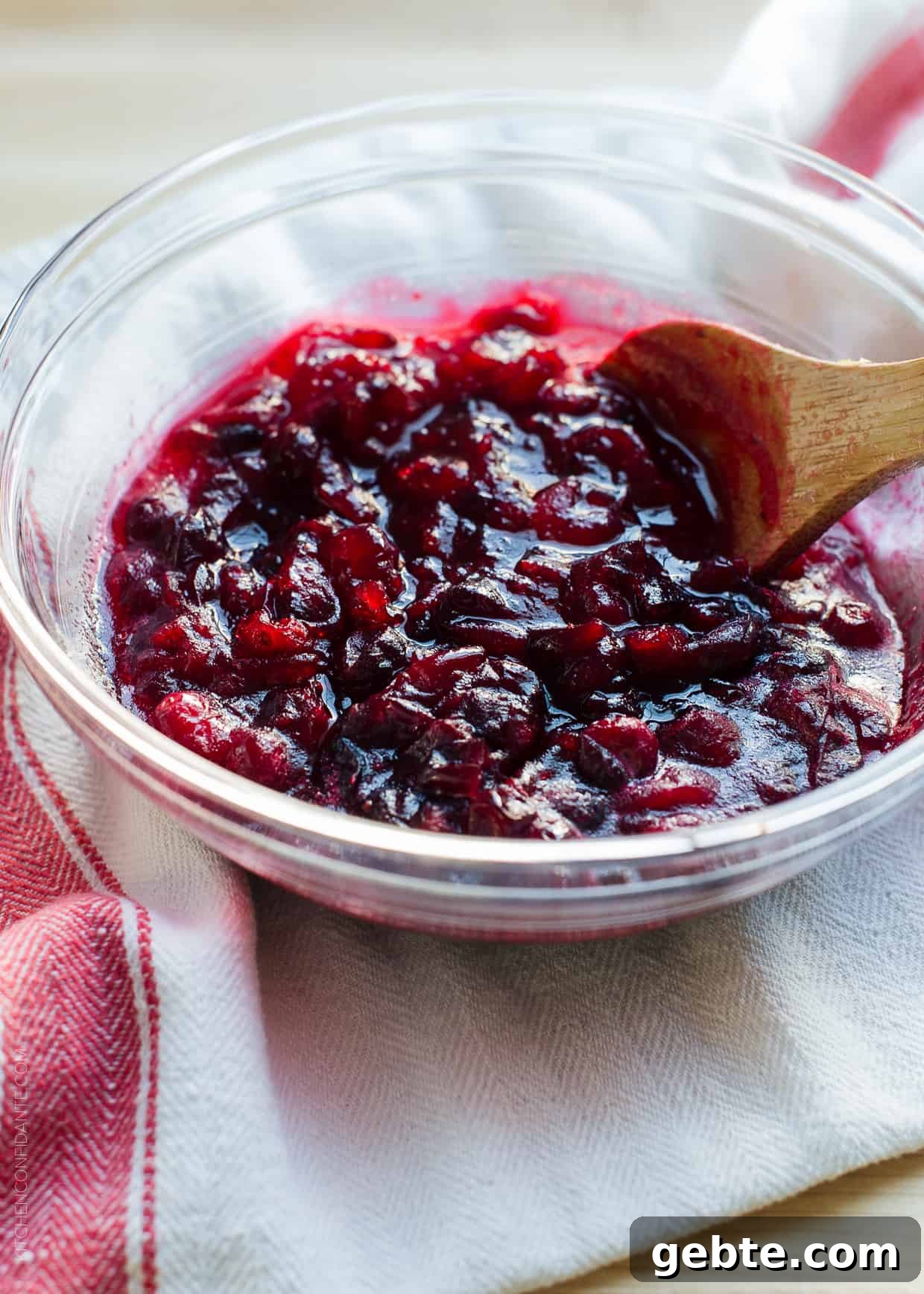 Cranberry Wine Sauce Recipe for Holiday Roasts and Sides 5 A wooden spoon stirring Cranberry Wine Sauce in a glass bowl.