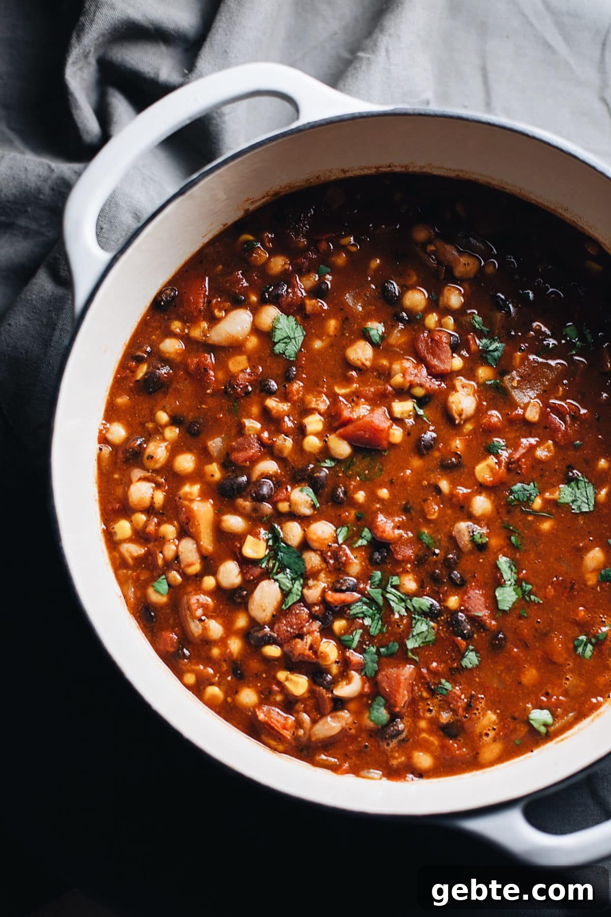 A white dutch oven with vegetarian bean chili in it.