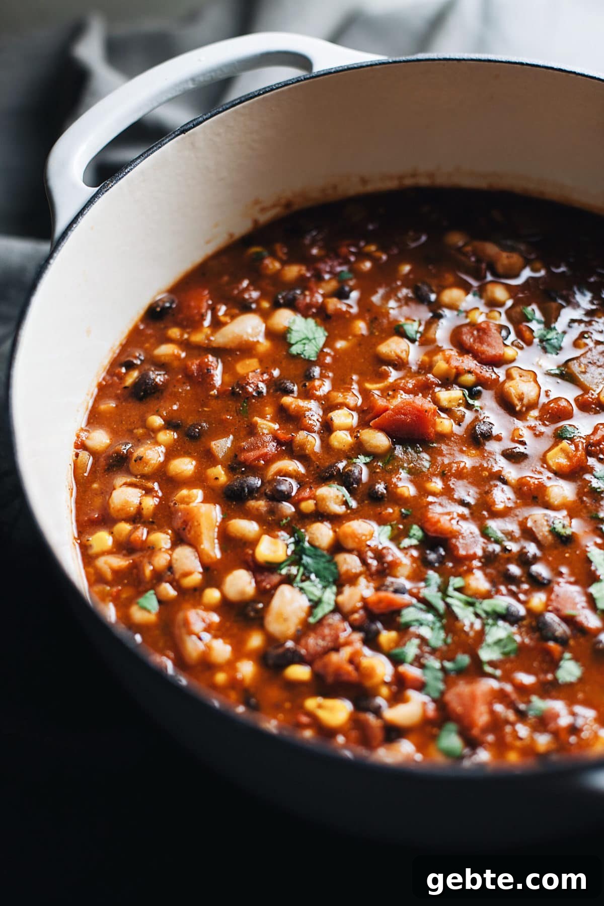 A white dutch oven with vegetarian bean chili in it.