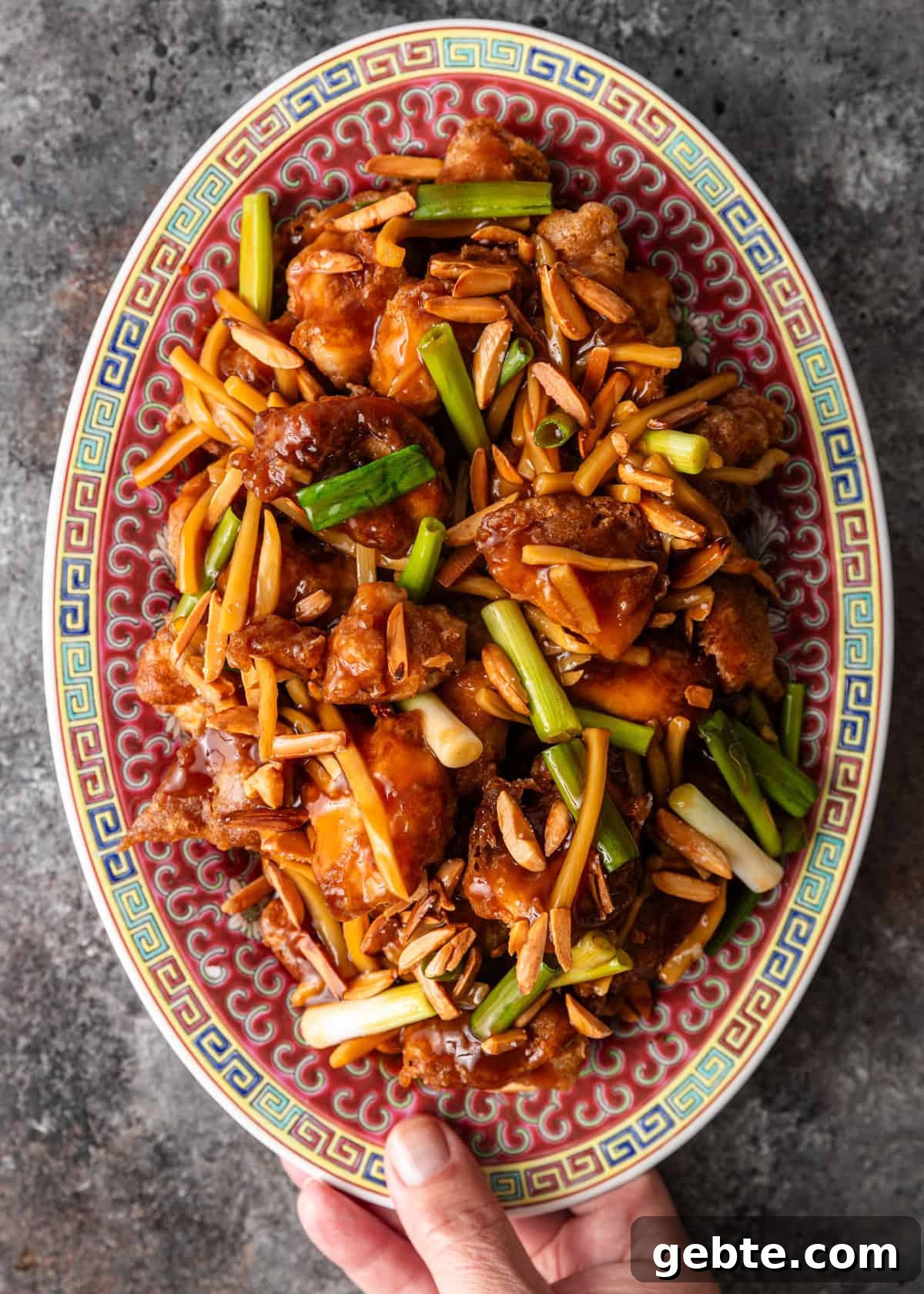 overhead: a hand holding a large ceramic serving platter full of my almond chicken recipe