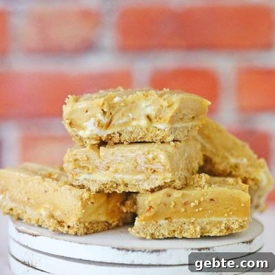 A few squares of no bake peanut butter fudge with cream cheese and a graham crust, stacked up on a wooden dessert plate