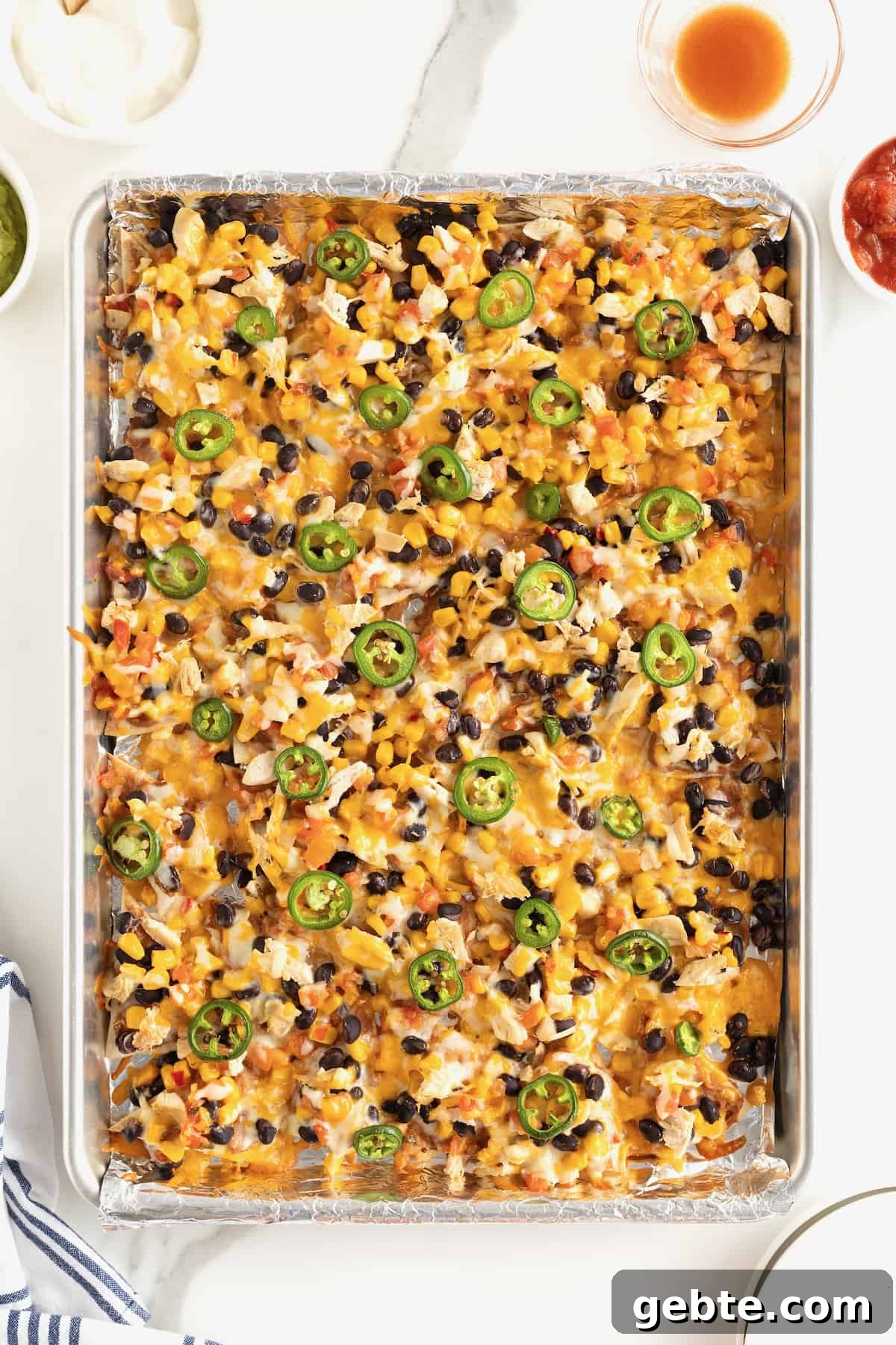 An aluminum sheet pan filled with nachos topped with cheese, black beans and jalapeño slices.