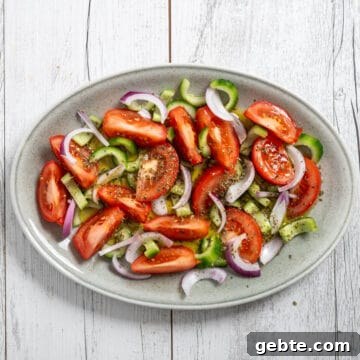 a greek cucumber tomato salad on an oval platter on a white table.
