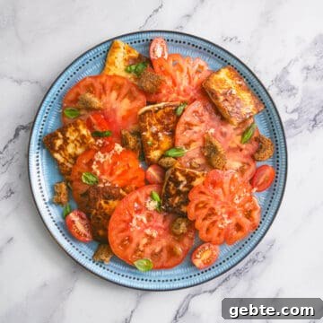 Blue plate with tomato and halloumi salad, topped with croutons and fresh basil.