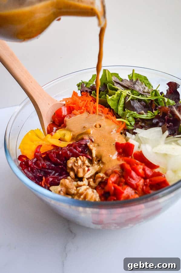 Pouring a creamy balsamic dressing onto a chopped salad in a glass bowl