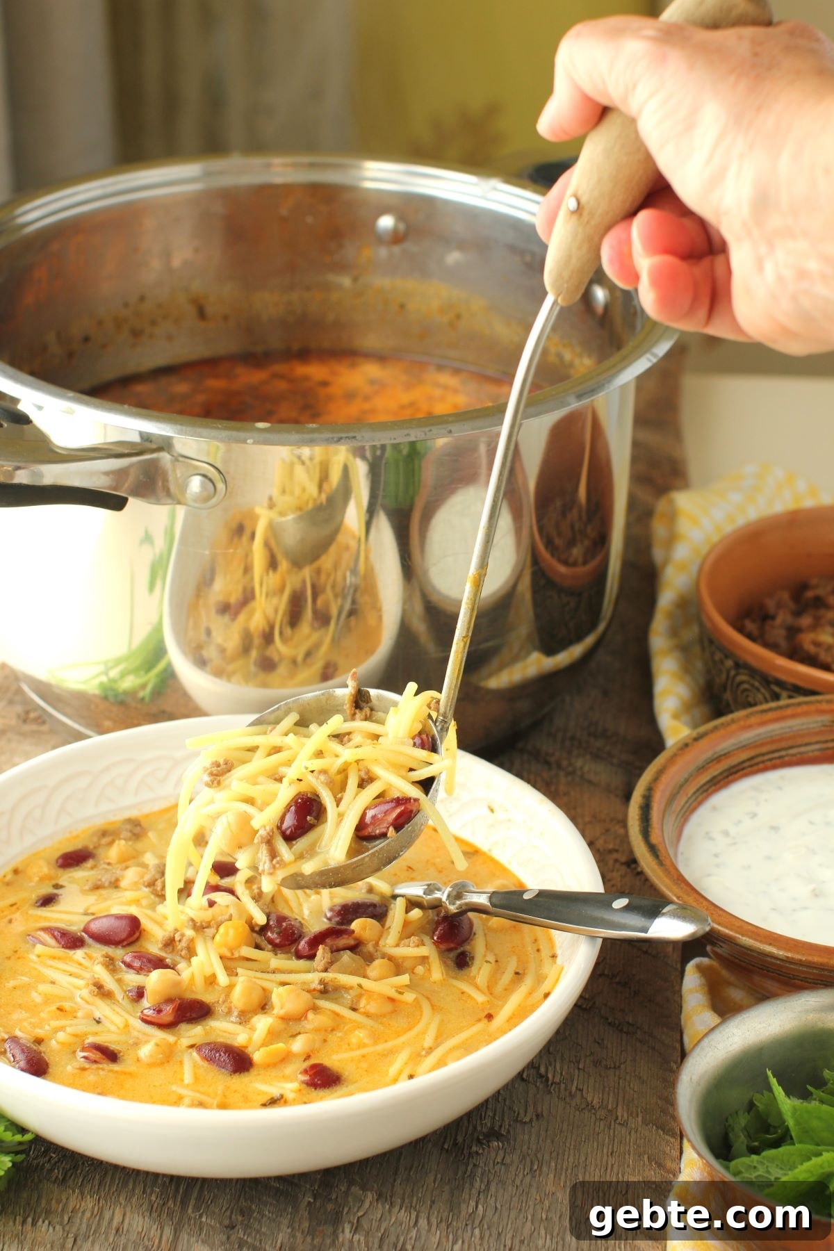 hand ladling aush noodles and beans into the bowl.