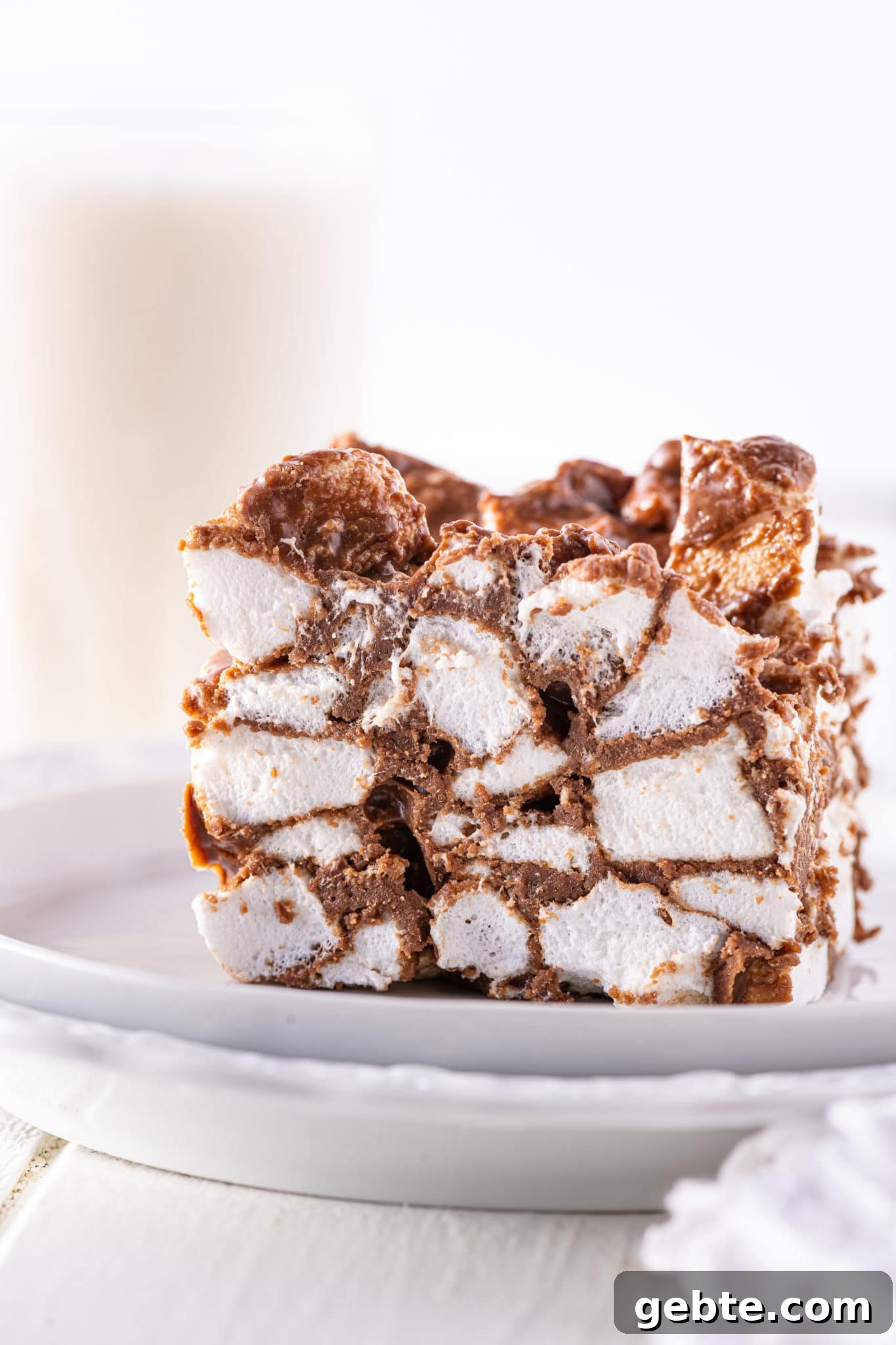 A single chocolate covered marshmallow bars with a tall glass of almond milk in the background, with a white napkin against a bright and airy background