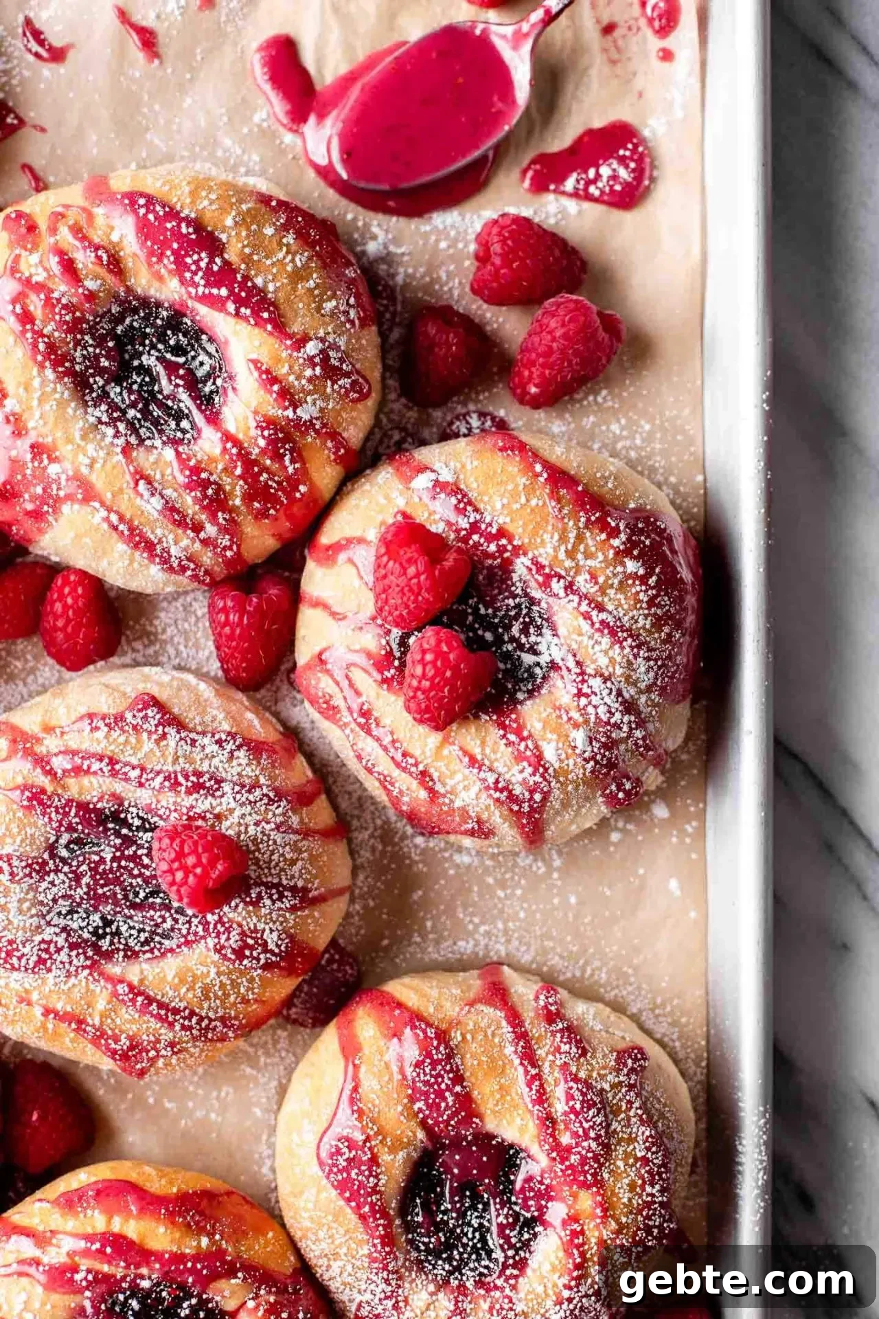 baked raspberry donuts on parchment lined baking sheet topped with icing and a light dusting of powdered sugar