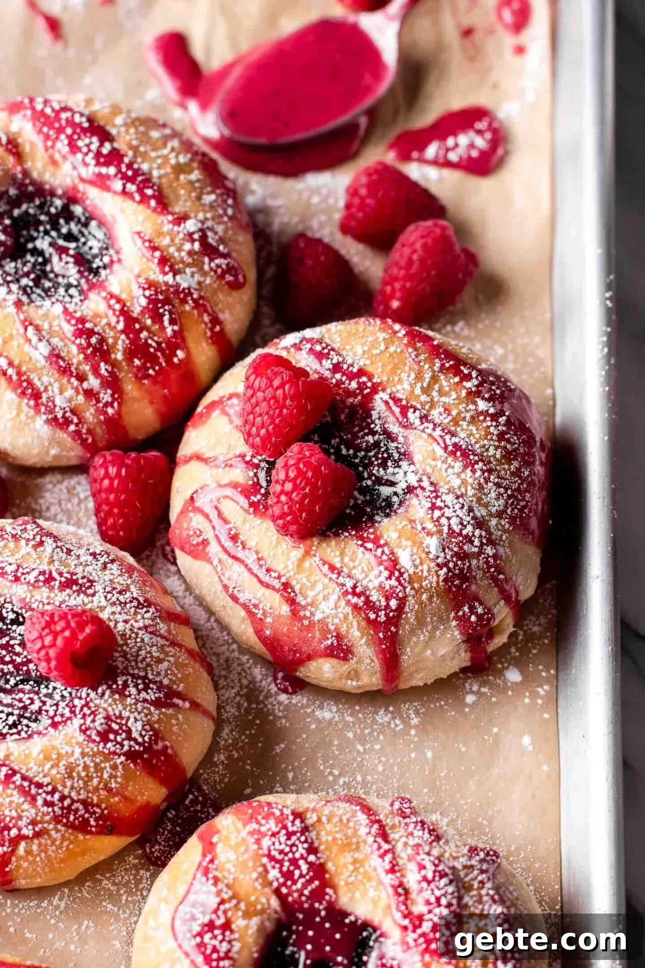 baked raspberry donuts on parchment lined baking sheet topped with icing and a light dusting of powdered sugar
