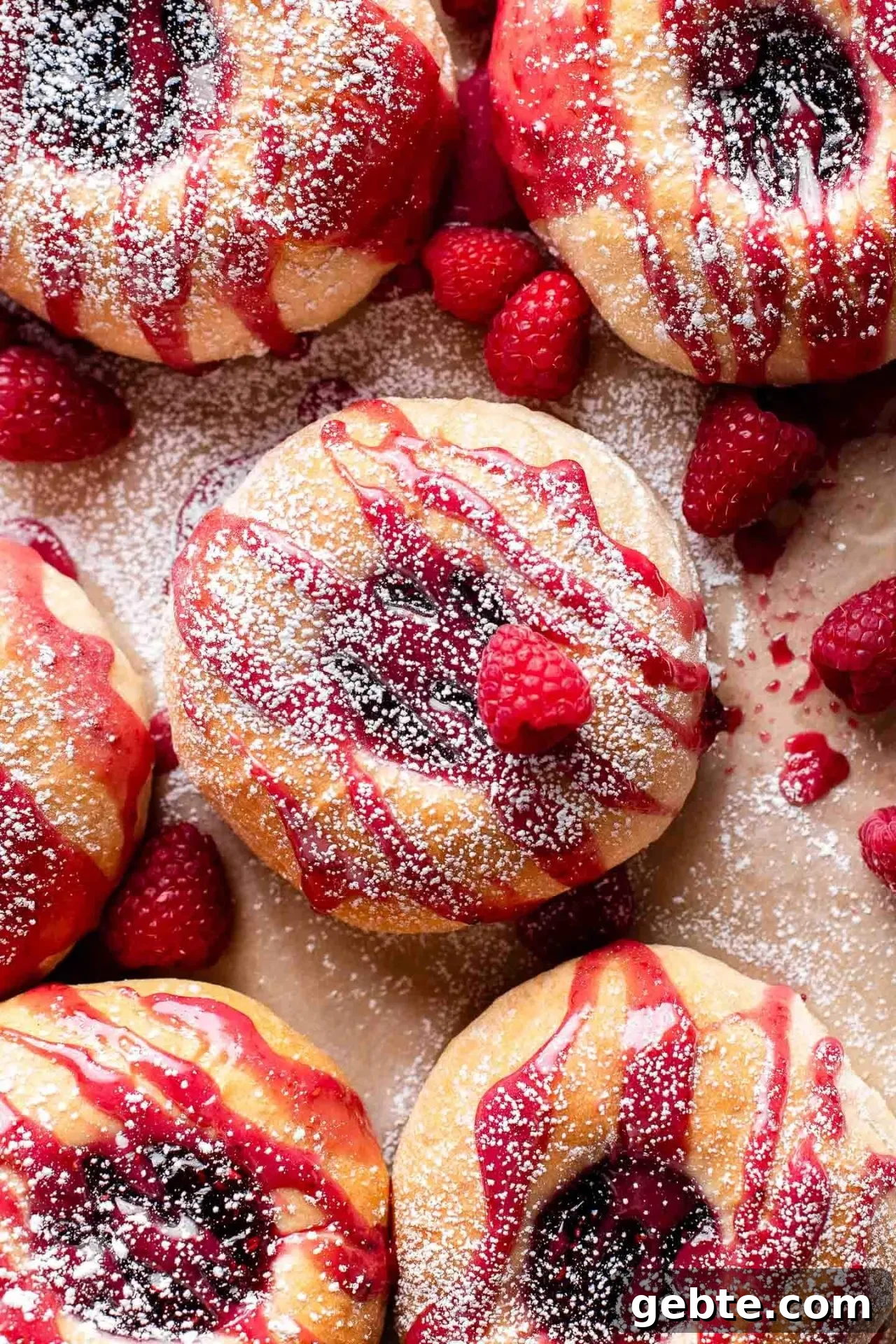 baked raspberry donuts on parchment lined baking sheet topped with icing and a light dusting of powdered sugar